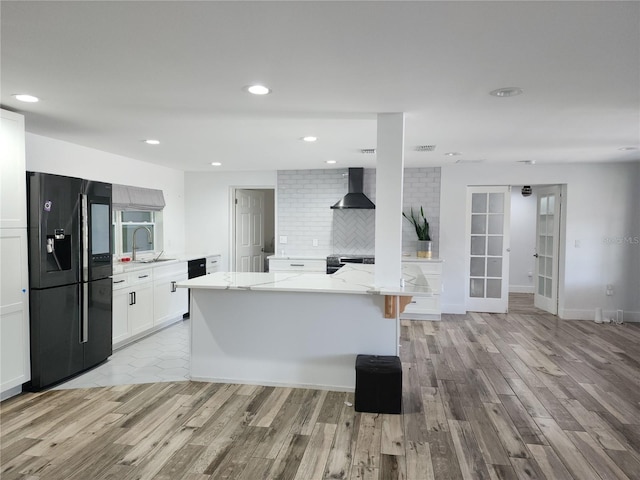 kitchen with a sink, wall chimney exhaust hood, light wood-type flooring, and black fridge