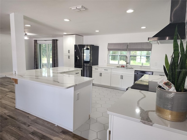 kitchen featuring a wealth of natural light, black fridge, a sink, a kitchen island, and wall chimney exhaust hood