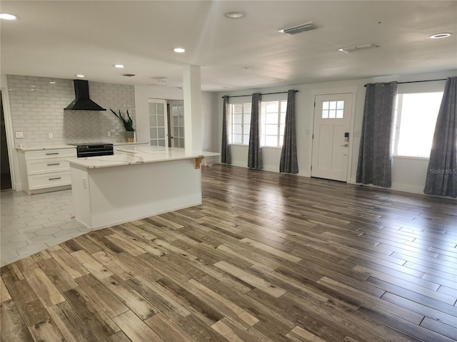 kitchen with visible vents, wood finished floors, black range with electric cooktop, wall chimney exhaust hood, and decorative backsplash