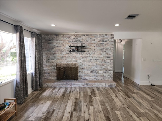 unfurnished living room featuring visible vents, a brick fireplace, a healthy amount of sunlight, and wood finished floors