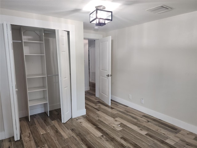 unfurnished bedroom featuring dark wood finished floors, baseboards, visible vents, and a closet