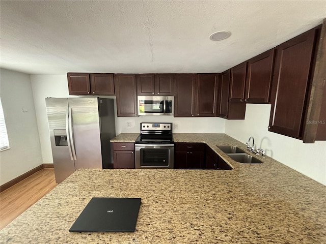 kitchen with a sink, a textured ceiling, stainless steel appliances, light wood finished floors, and dark brown cabinets