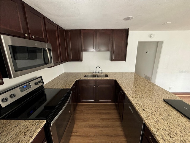 kitchen featuring a sink, light stone countertops, appliances with stainless steel finishes, and dark wood-style flooring