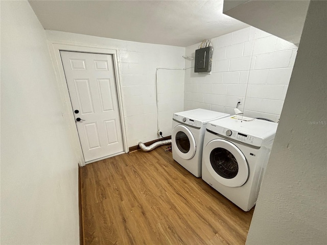 washroom featuring electric panel, washer and dryer, light wood-type flooring, and concrete block wall