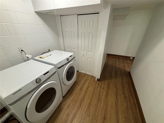 clothes washing area with concrete block wall, dark wood-style floors, baseboards, laundry area, and washing machine and dryer