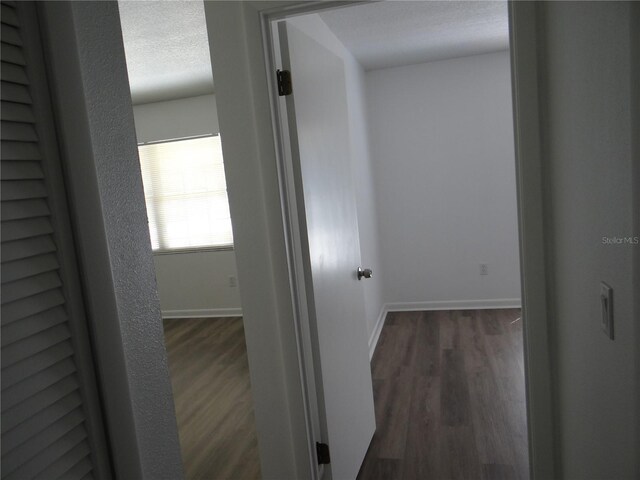 hall featuring baseboards, a textured ceiling, and dark wood-style flooring