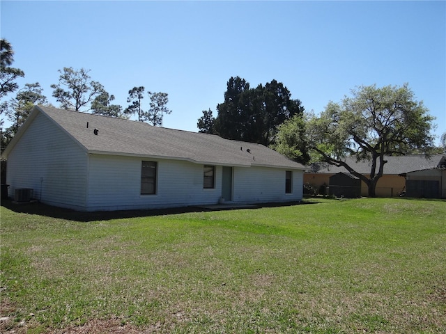 back of house featuring a yard, cooling unit, and a shingled roof