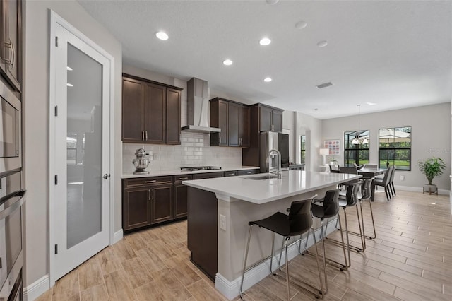 12654 Oak Hill Way, Parrish, FL 34219 - kitchen featuring wall chimney range hood, dark brown cabinets, a kitchen island with sink, light countertops, and a breakfast bar area