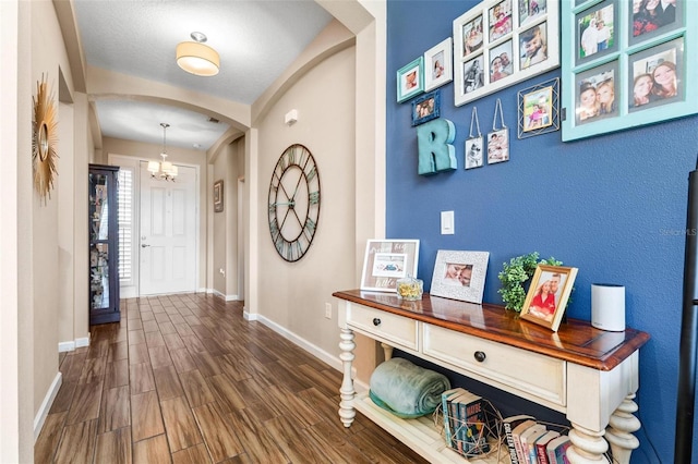 entryway featuring baseboards, arched walkways, dark wood-type flooring, and a chandelier