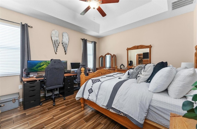 bedroom with a ceiling fan, a raised ceiling, wood finished floors, and visible vents