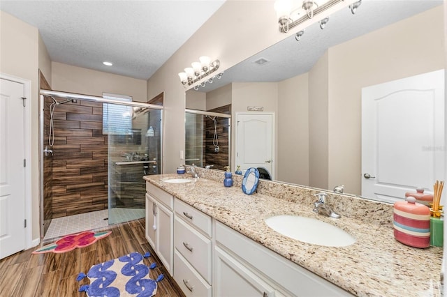 full bath with a textured ceiling, wood finish floors, a stall shower, and a sink