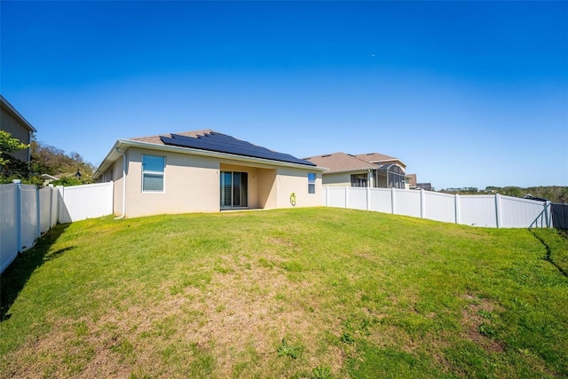 rear view of house featuring a fenced backyard, roof mounted solar panels, stucco siding, and a yard