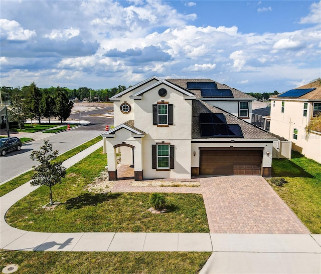 view of front of home featuring solar panels, a front lawn, roof with shingles, stucco siding, and decorative driveway