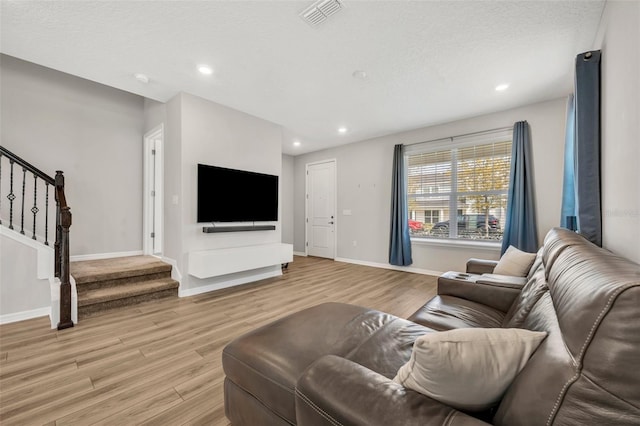 living room featuring visible vents, baseboards, light wood-style floors, and stairs