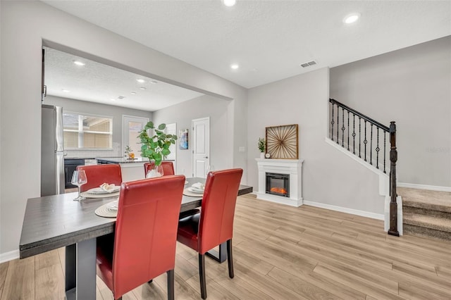 dining area with light wood finished floors, baseboards, stairs, a glass covered fireplace, and a textured ceiling