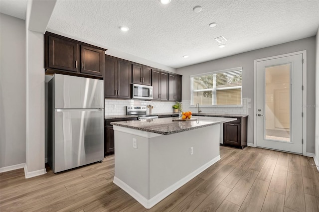 kitchen with dark stone countertops, a center island, stainless steel appliances, light wood finished floors, and dark brown cabinets