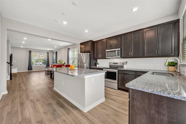 kitchen featuring dark brown cabinetry, decorative backsplash, light wood-style flooring, appliances with stainless steel finishes, and a sink