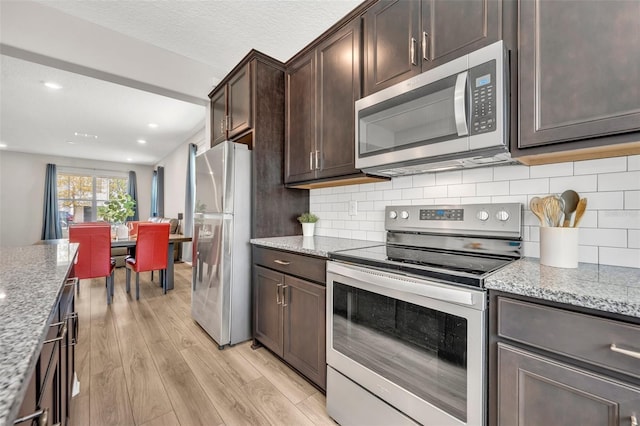 kitchen featuring light stone counters, light wood-style flooring, stainless steel appliances, dark brown cabinetry, and backsplash