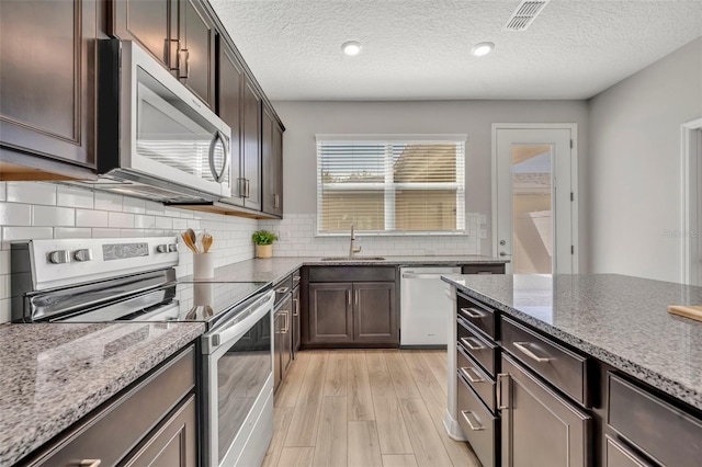 kitchen featuring visible vents, a sink, dark brown cabinets, light wood-style floors, and appliances with stainless steel finishes