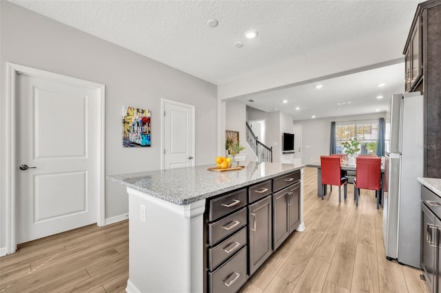 kitchen featuring light stone counters, a kitchen island, a textured ceiling, freestanding refrigerator, and light wood-style floors