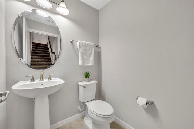 half bathroom featuring tile patterned floors, toilet, baseboards, and a sink