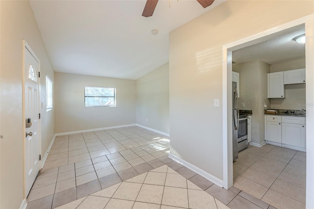 empty room featuring light tile patterned floors, a ceiling fan, vaulted ceiling, and baseboards