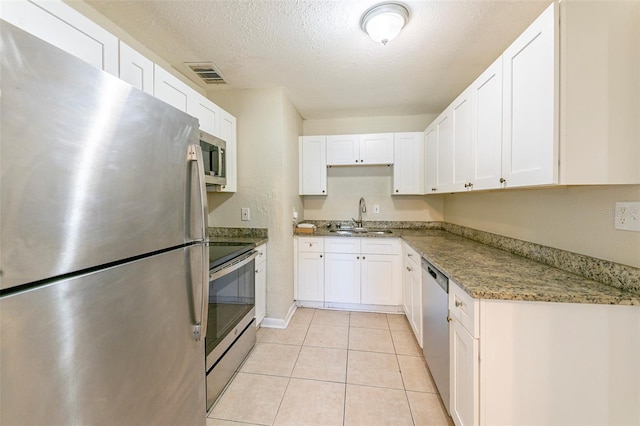kitchen with light stone counters, appliances with stainless steel finishes, white cabinets, a sink, and visible vents