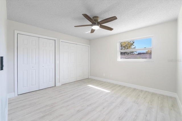 unfurnished bedroom with light wood-style flooring, a textured ceiling, two closets, and baseboards