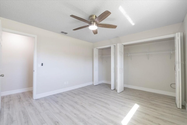 unfurnished bedroom featuring light wood-style floors, baseboards, two closets, and a textured ceiling