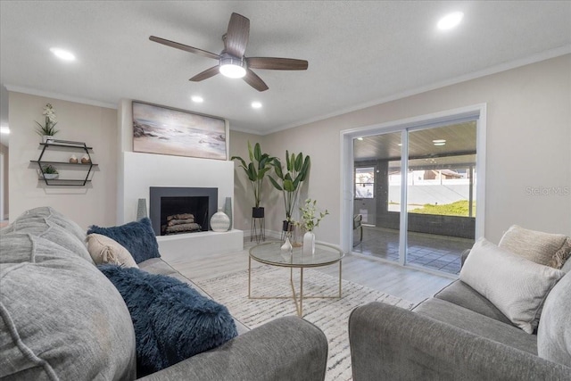 living area with recessed lighting, wood finished floors, a large fireplace, and ornamental molding