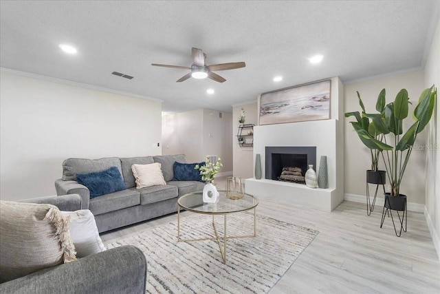 living area featuring visible vents, a fireplace with raised hearth, crown molding, baseboards, and wood finished floors