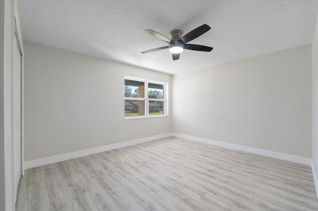 spare room featuring a ceiling fan, baseboards, light wood finished floors, and a textured ceiling