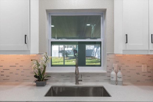 room details with a sink, light stone counters, tasteful backsplash, and white cabinetry