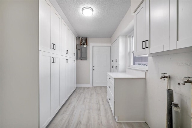 washroom featuring electric panel, cabinet space, a textured ceiling, and light wood-style flooring