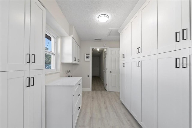 laundry room featuring light wood-type flooring, visible vents, baseboards, and a textured ceiling