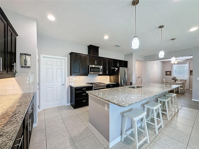 kitchen with visible vents, backsplash, a center island with sink, appliances with stainless steel finishes, and a kitchen breakfast bar