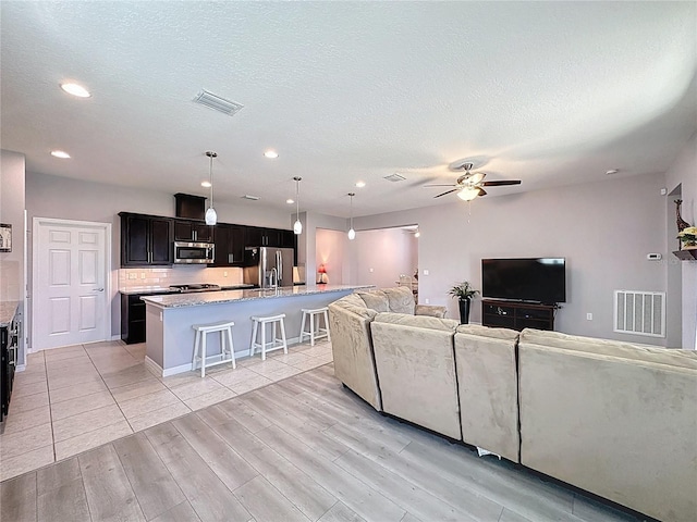 living area with visible vents, light wood-style floors, a ceiling fan, and a textured ceiling