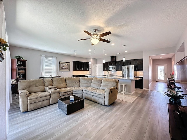 living room with a textured ceiling, light wood-type flooring, and ceiling fan