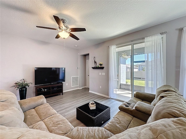 living area featuring visible vents, a textured ceiling, wood finished floors, and a ceiling fan