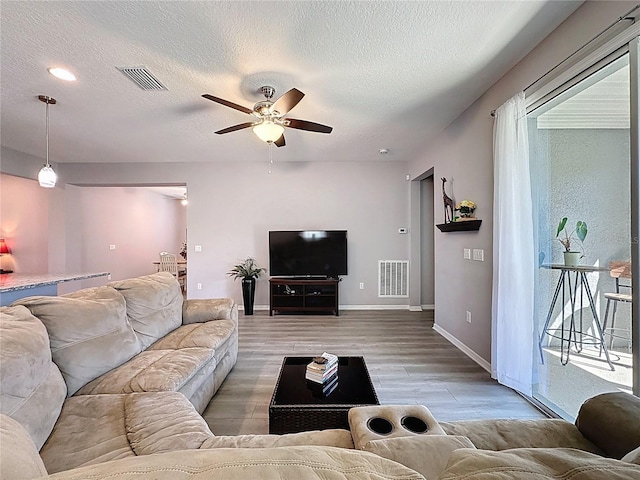 living area with light wood finished floors, visible vents, a textured ceiling, and ceiling fan