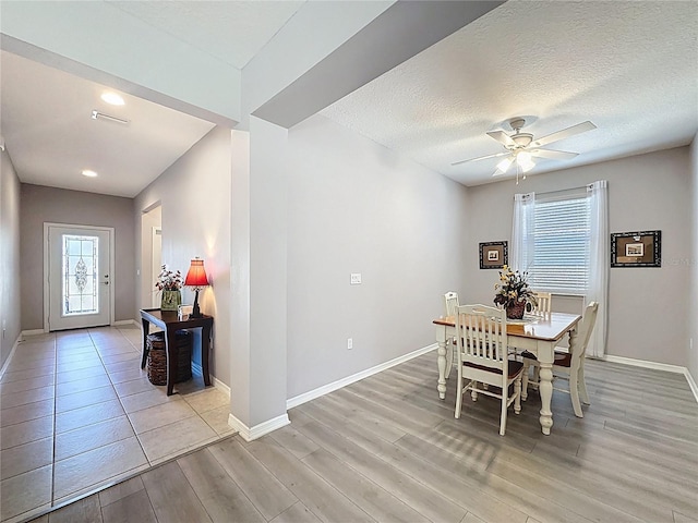 dining area featuring light wood-style flooring, a textured ceiling, baseboards, and ceiling fan