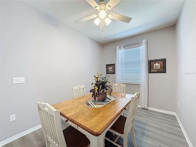 dining area featuring baseboards, light wood-style floors, ceiling fan, and a textured ceiling