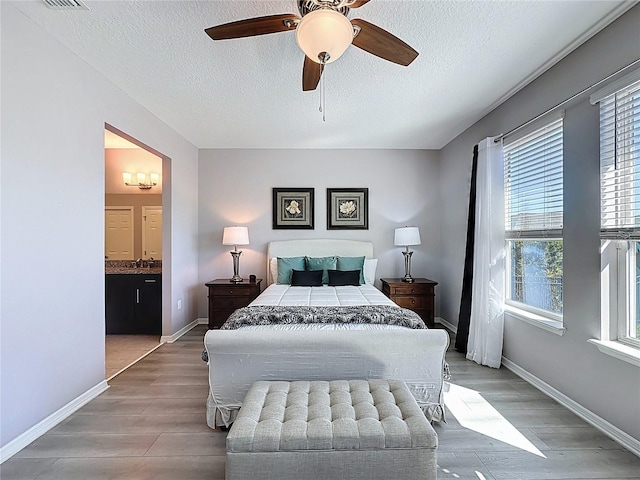 bedroom featuring light wood-type flooring, a textured ceiling, connected bathroom, baseboards, and ceiling fan