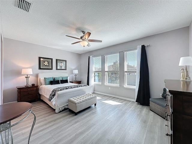 bedroom with visible vents, baseboards, light wood-type flooring, a textured ceiling, and a ceiling fan