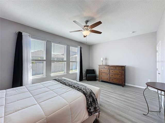 bedroom with ceiling fan, a textured ceiling, light wood-type flooring, and baseboards