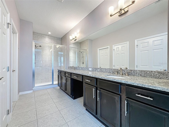 bathroom featuring double vanity, a stall shower, tile patterned floors, a textured ceiling, and a sink