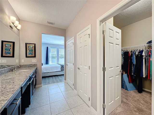 ensuite bathroom featuring tile patterned floors, visible vents, a textured ceiling, and vanity