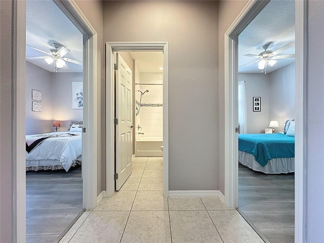 hallway with light tile patterned floors, baseboards, and a textured ceiling