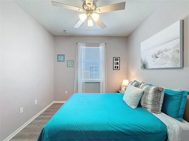 bedroom with a textured ceiling, a ceiling fan, baseboards, and wood finished floors