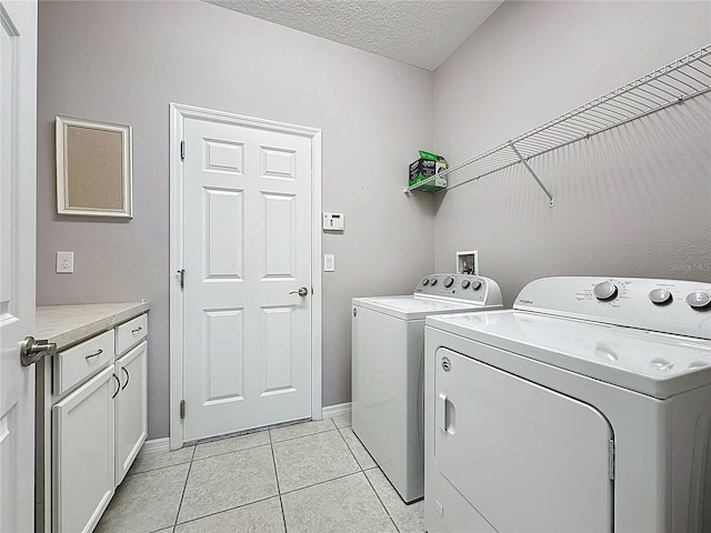 laundry area with a textured ceiling, cabinet space, separate washer and dryer, light tile patterned floors, and baseboards